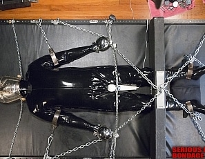 R662_MALEBONDAGE-Chain101_Wired4Fun_BootedRay_Mark_InRubberOnBondageTableWithHeadBoxFrontRoom