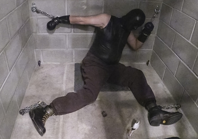 R938_MALEBONDAGE_BondageSittingAtEdgeDungeon_MarkShaneSeth_MarkChainedToWallInSolitaryCell